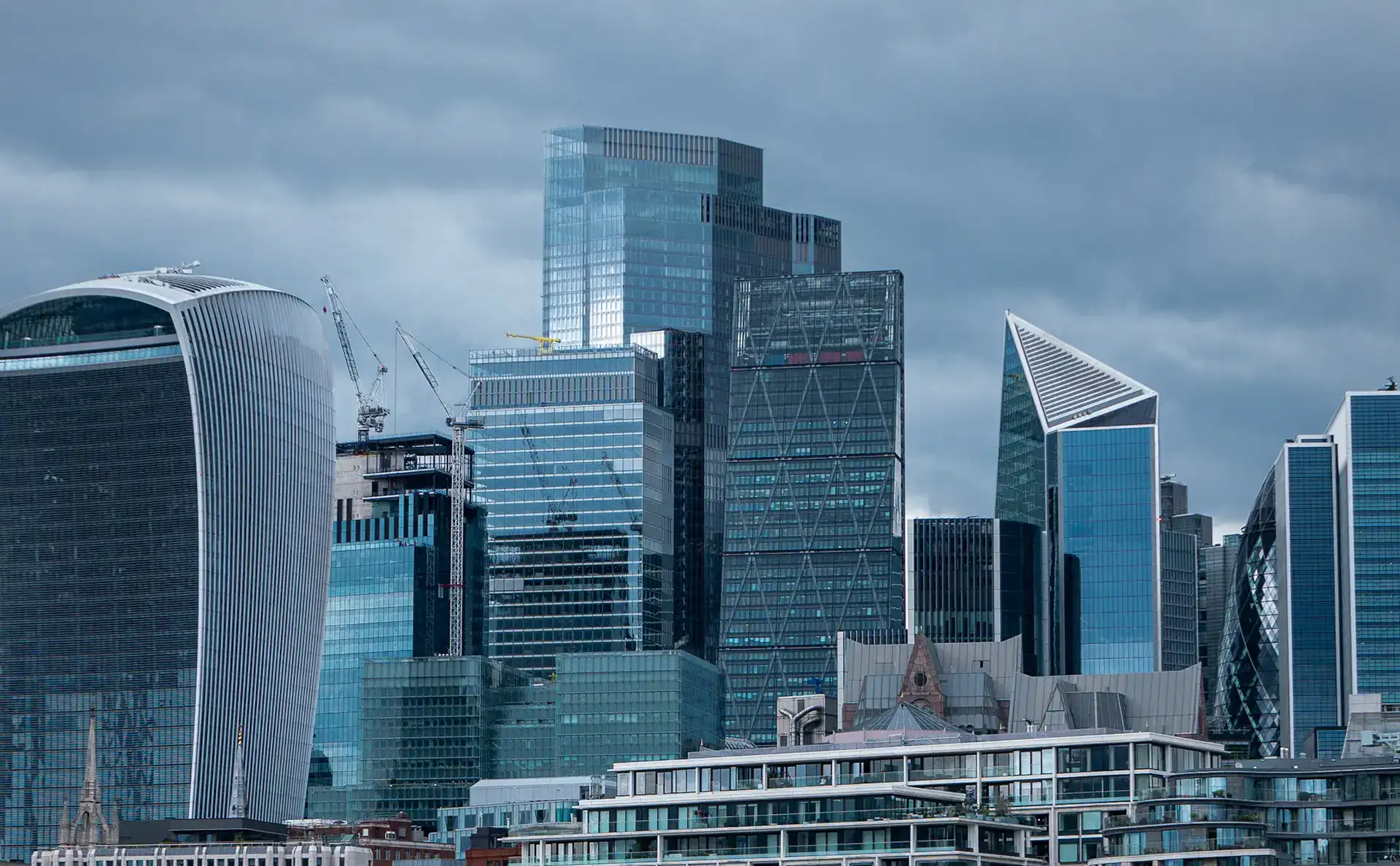 Modern glass skyscrapers in London financial district, featuring innovative architecture and construction cranes.