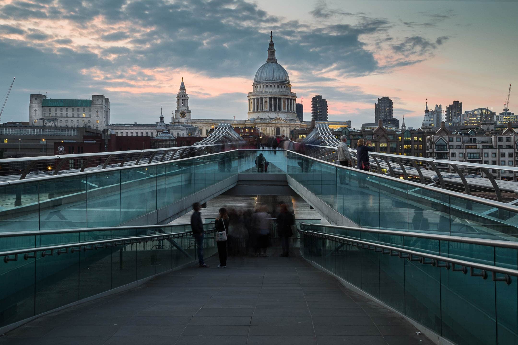 Modern London Millennium Bridge with St. Paul's Cathedral skyline at sunset.