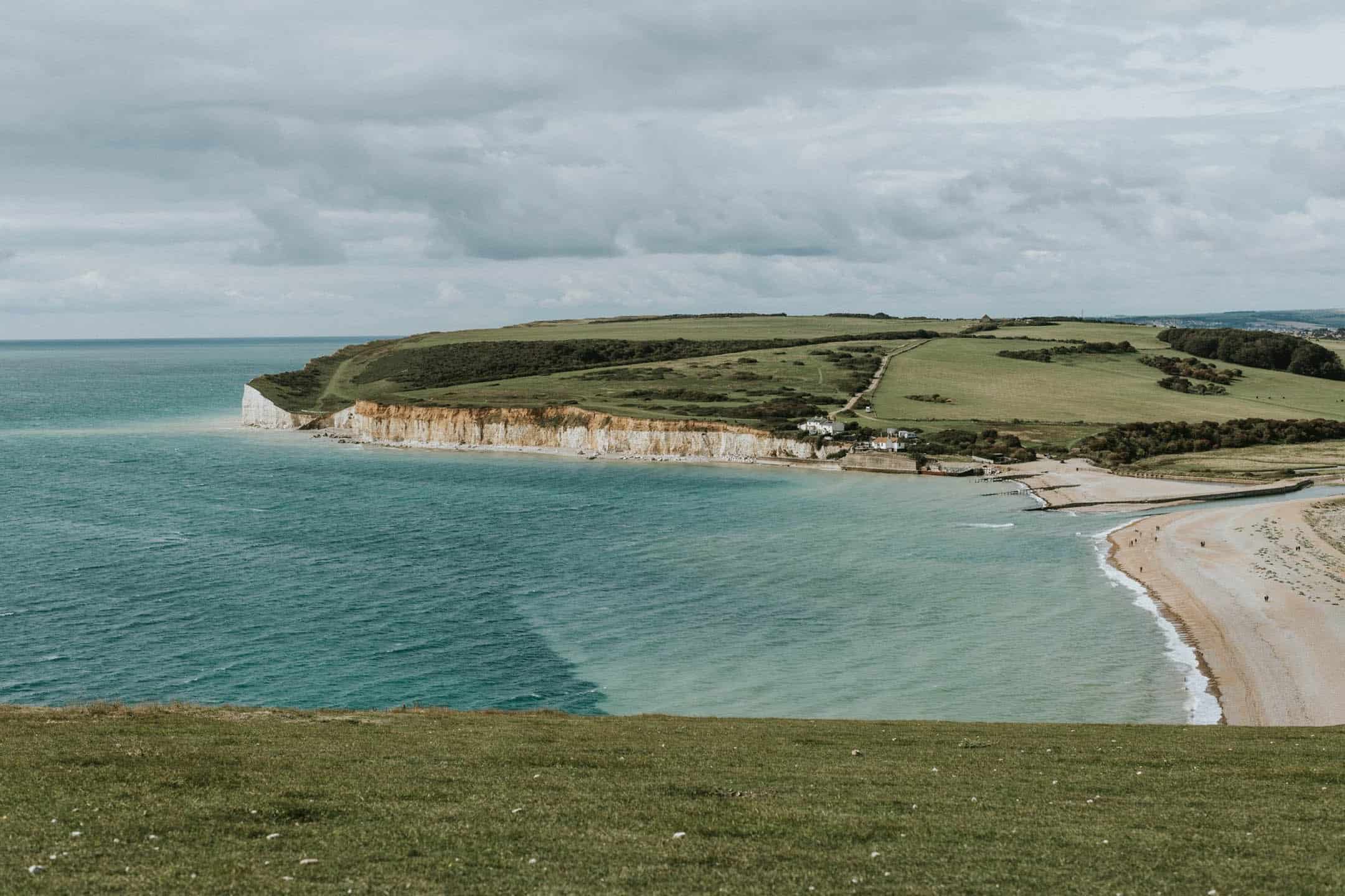 Cliffs and beach on the South Coast of England with green fields and ocean views.