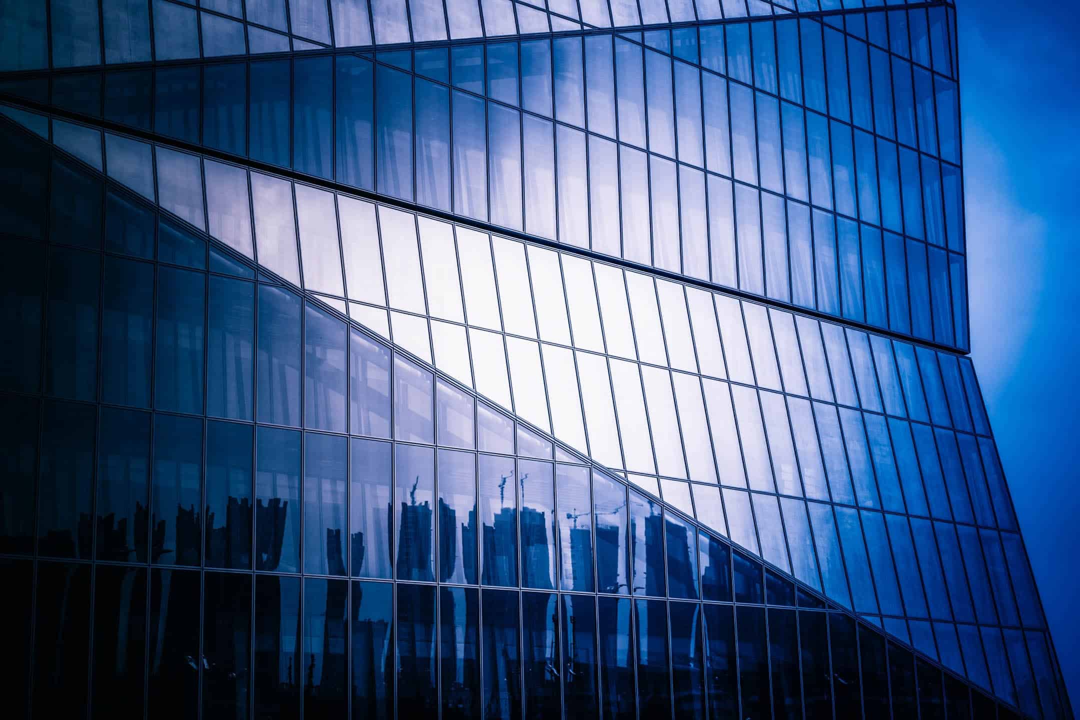 Contemporary glass office building with reflective windows, modern architecture, blue sky, cityscape reflection.